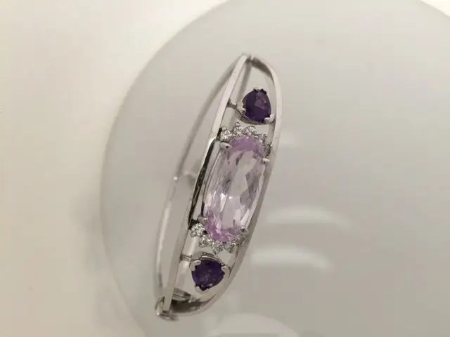 A close-up view of a silver ring with two oval-shaped purple gemstones and a larger oval-shaped purple gemstone in the center