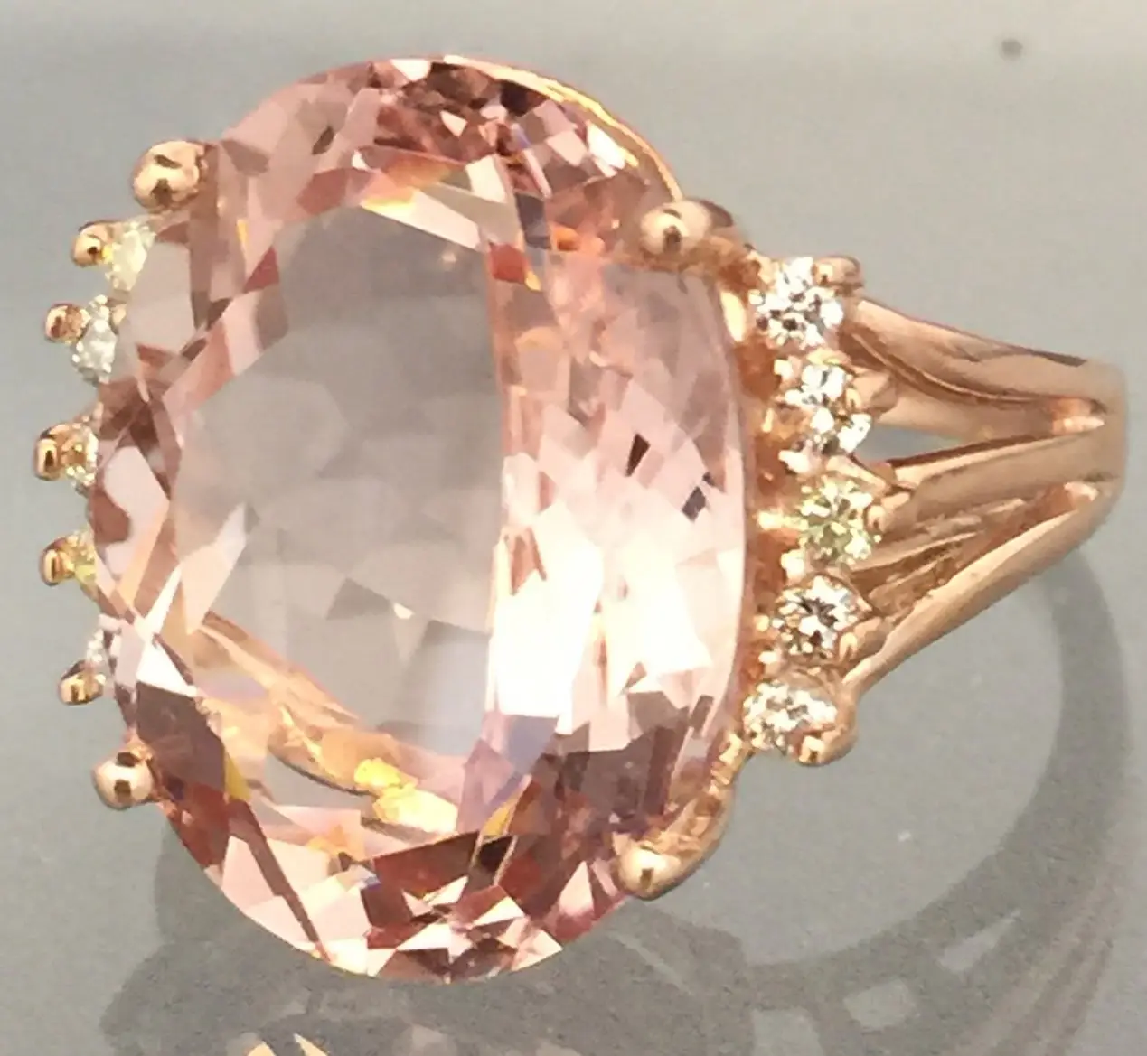 A close-up view of a rose gold ring with a large oval-shaped peach-colored gemstone in the center, surrounded by smaller clear gemstones