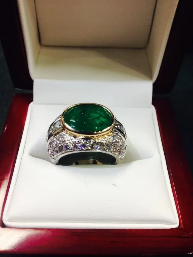 A close-up view of a silver ring with a large oval-shaped green gemstone in the center, surrounded by smaller clear gemstones