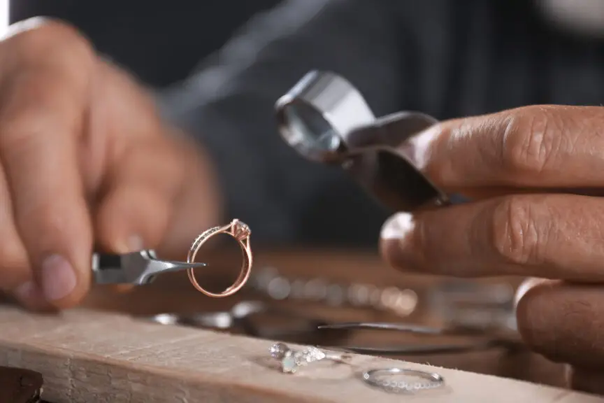 A person's hand holding a pair of pliers and working on a piece of jewelry.