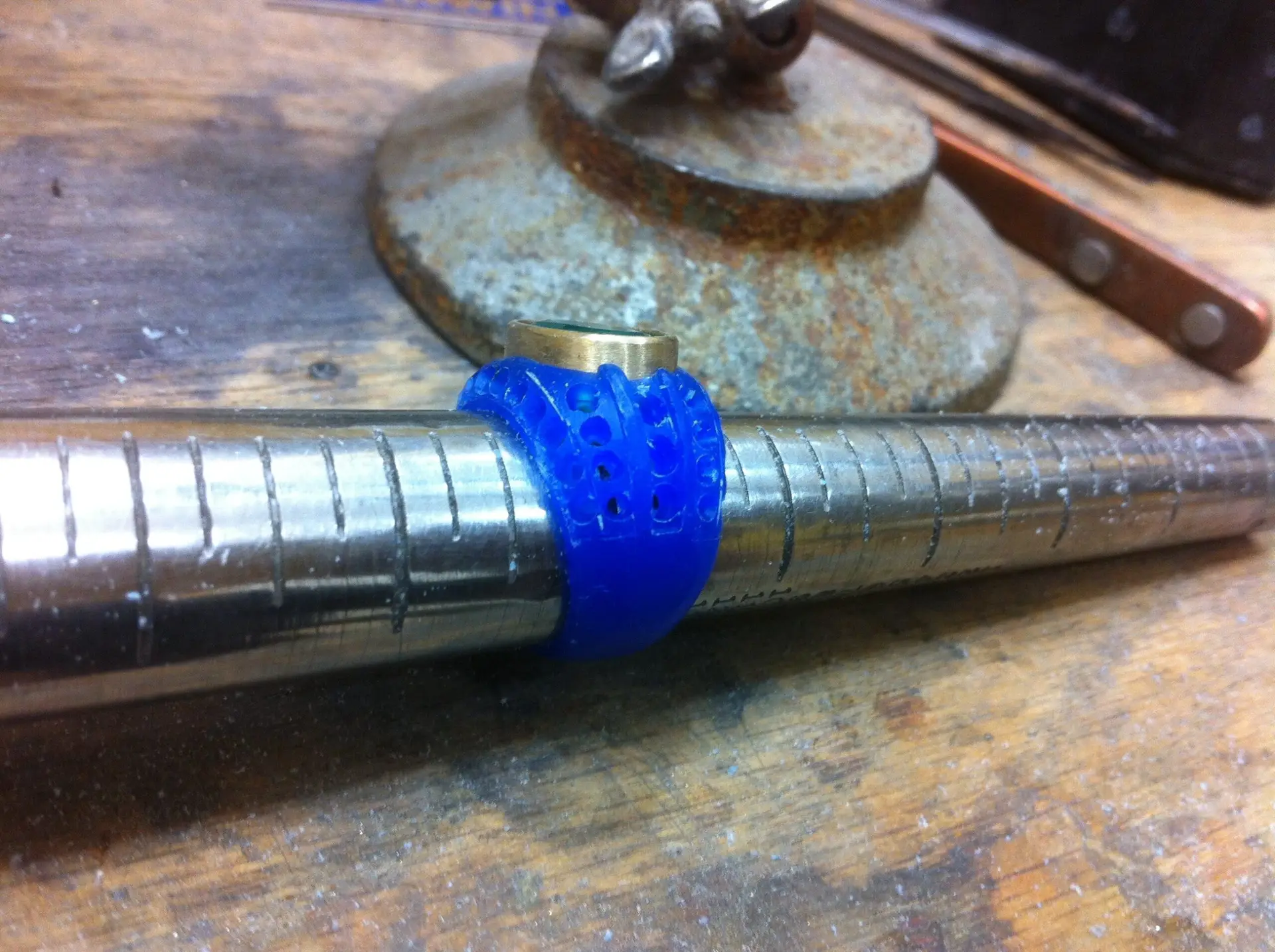 A metal pipe with a blue plastic piece attached to it, sitting on a wooden surface along with what appears to be a grinding tool
