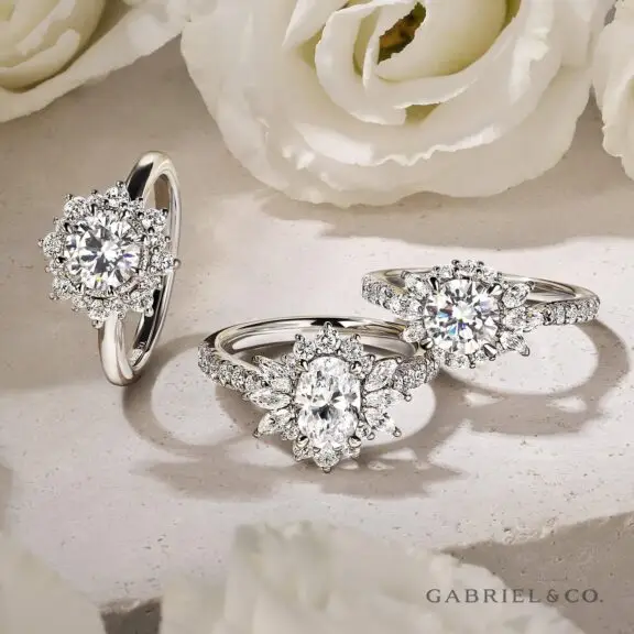 Three diamond engagement rings set with round brilliant diamonds and accented with smaller diamonds on a light background.