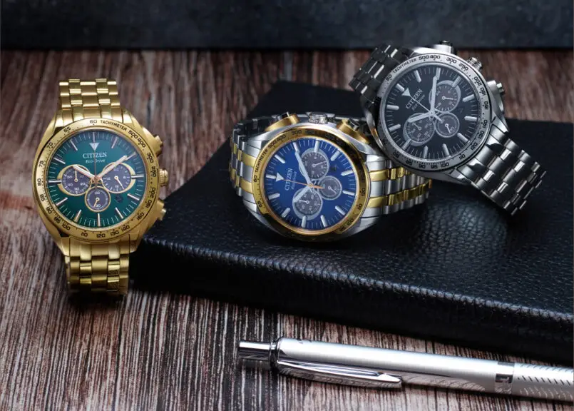 Several watches displayed on a black leather surface, including gold and silver toned models with chronograph features