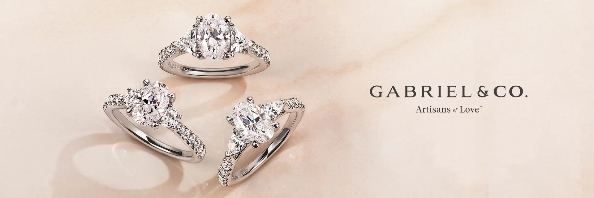Several diamond rings in various styles and shapes, including solitaire, halo, and side stone designs, displayed on a light background with the GABRIEL & CO. logo.