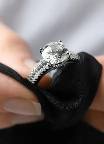 A close-up view of a diamond engagement ring with a round brilliant center diamond set in a halo of smaller diamonds on a woman's hand.